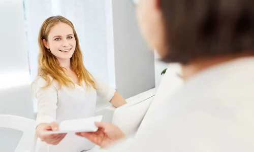 Eine MFA überreicht einer Patientin eine Überweisung